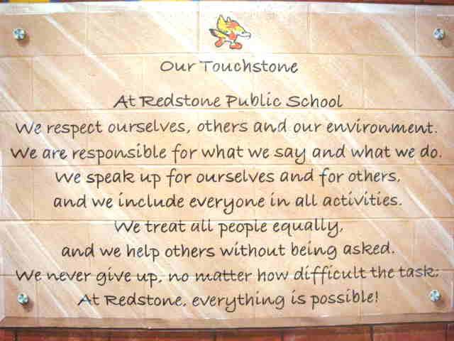 text of the school touchstone appears on a clear plaque in front of a wall.